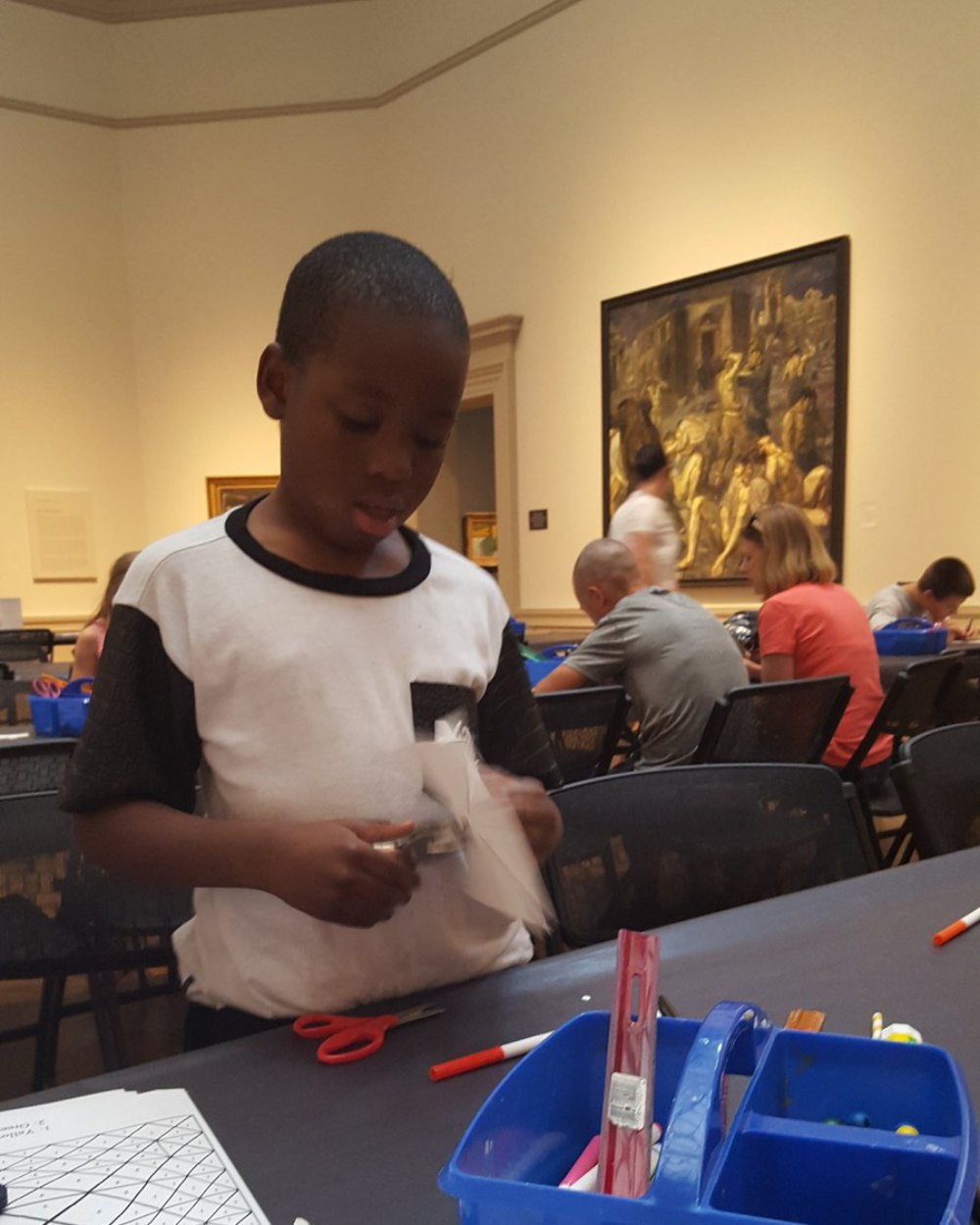 A young artist cutting paper shapes during a SIP Arts session in a museum gallery.
